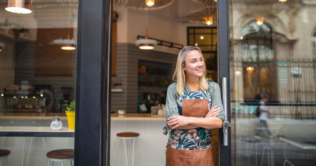 Jonge cafe eigenaar staat met haar armen gekruist bij de voordeur