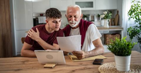 Grootvader en kleinzoon bestuderen samen thuis financiële documenten.